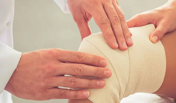 A woman holding her knee in pain, showing signs of a dislocated knee joint